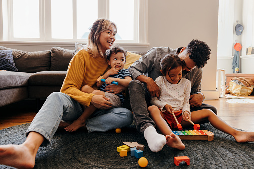Young parents playing with their son and daughter in the living room. Mom and dad having fun with their children during playtime. Family of four spending some quality time together at home.