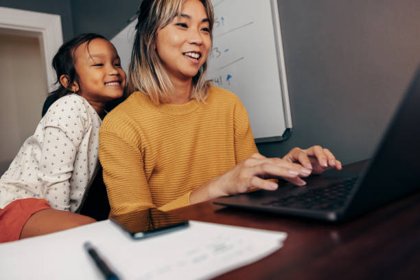 niña feliz viendo a su madre trabajar en una computadora portátil - working mother working mother balance fotografías e imágenes de stock