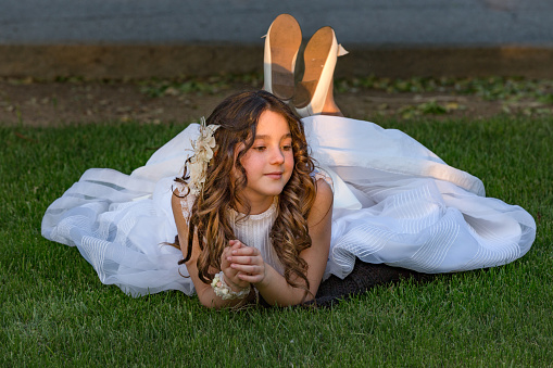 Madrid Spain. May 5, 2018. Smiling young girl wearing communion dress lying on the grass at sunset