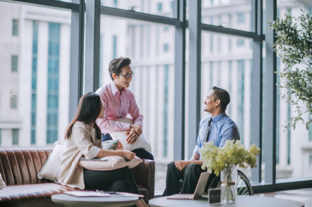 Indian male white collar worker in wheelchair discussion in office lounge with his colleague Indian male white collar worker in wheelchair discussion in office lounge with his colleague asian stock pictures, royalty-free photos & images