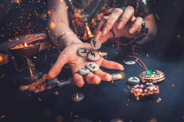 Astrology and esotericism. The witch puts the rune stones in his hand, standing next to the candle. Sparks of fire in the air. Dark background. Astrology and esotericism. The witch puts the rune stones in his hand, standing next to the candle. Sparks of fire in the air. Dark background. Copy space. runes stock pictures, royalty-free photos & images