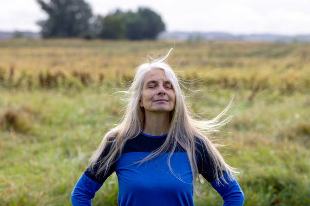 Mature woman doing Yoga outdoors in France while on a wellness vacation. She is sitting on the ground practising breathing with her eyes closed.