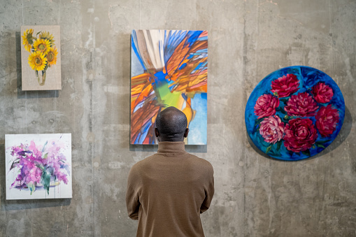Vista trasera del invitado masculino africano de la galería de arte de pie frente a la pared con exposiciones photo