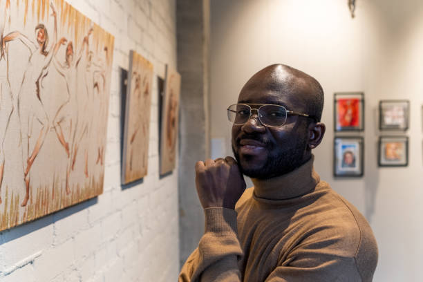 istock Happy young African man looking at you while standing by wall with artworks 1365119172