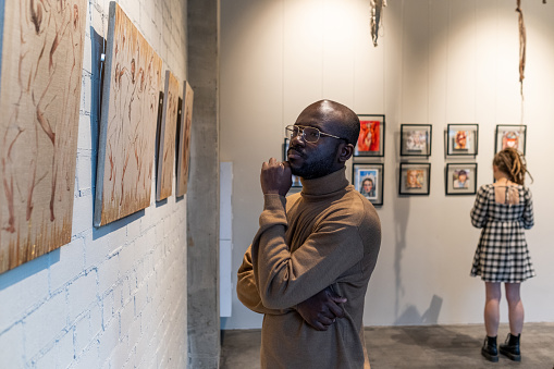 Hombre africano serio en jersey marrón mirando la pintura photo