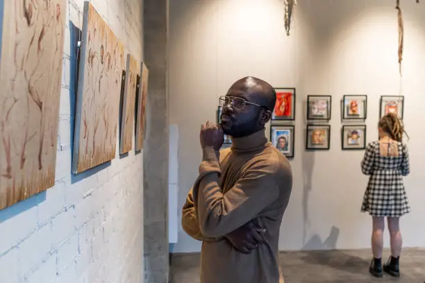 Photo of Serious African man in brown pullover looking at painting