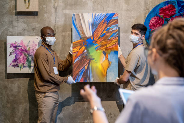 istock Two gallery workers in gloves and protective masks holding abstract painting 1365119766