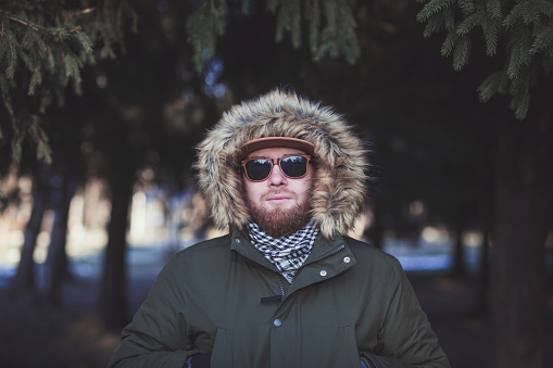 stylish man in sunglasses and winter jacket with fur hood