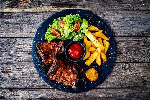 Grilled ribs, French fries and tomato salad on black wooden table