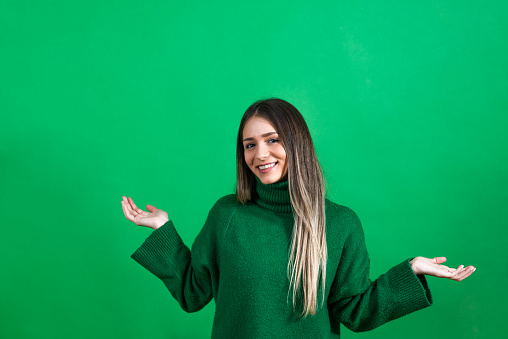 Portrait of positive cheerful woman promoter hold hand present ads promo object wear green sweater over green color not isolated background. Happy young female wondering pose looking at camera.