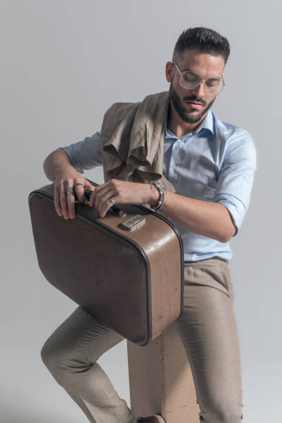istock cool young man with jacket over shoulder holding suitcase on thigh 1365128650