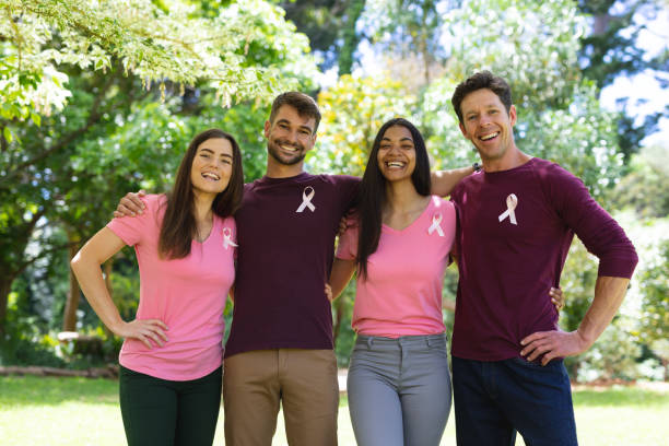 Portrait of smiling multiracial men and women wearing breast cancer awareness ribbons in park stock photo