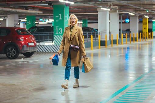 Young woman on walking in underground garage after shopping. A beautiful woman holding and showing shopping bags in the mall parking lot. Woman carries shopping bags