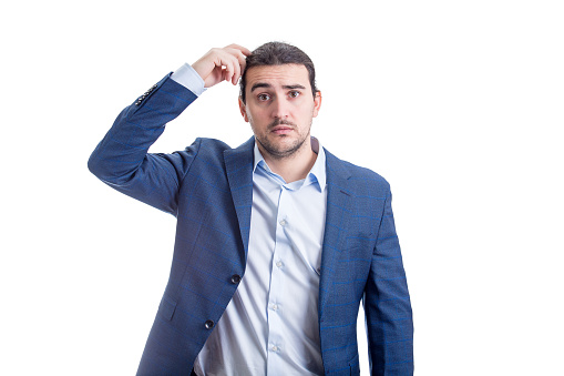 Clueless and pensive businessman scratching his head thinking of new ideas and solutions. Puzzled male looks confused and lost isolated on white background