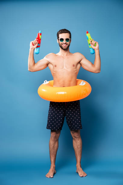 istock Cheerful man looking camera while holding water guns isolated 1365135216