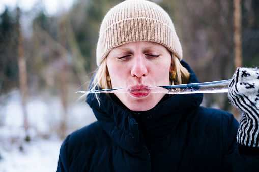 Cute woman in knit hat enjoying an ice-cold icicle outside in the snow.