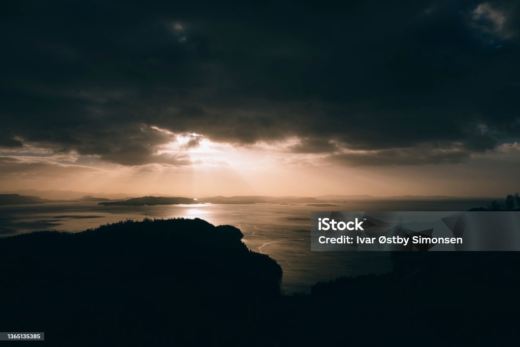 Sunset over a Norwegian fjord. Beautiful textures from the wind on the water View over a Norwegian fjord in with sunbeam breaking through heavy clouds. Rogaland County Stock Photo