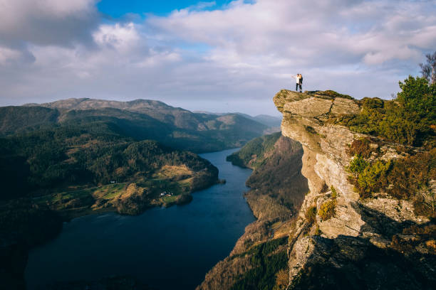 Man enjoying the view from a breathtaking viewpoint "Himakånå" in western Norway. Himakånå in Nedstrand is often called "Little Trolltunga". It is a scenic and spectacular cliffs rock formation with a great view over a fjord-like sea. observation point stock pictures, royalty-free photos & images