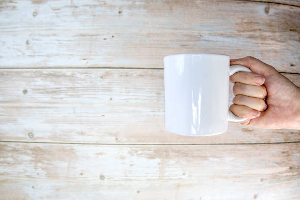 istock Hand holding a ceramic mug blank on wooden background with copy space, 1365135413