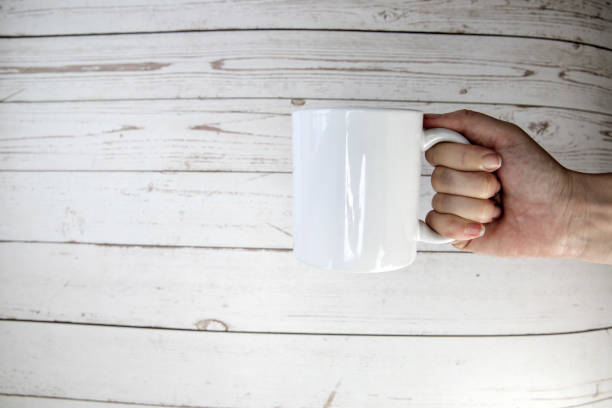 istock Hand holding a ceramic mug blank on wooden background with copy space, 1365135436