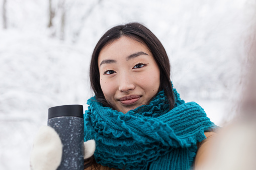 Close-up photo of young beautiful asian girl looking at camera phone, video call to girlfriend walking in winter snowy park