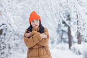 若いアジアの女の子は、暖かい服を着て、冬の雪の日に、デートを待って公園で凍結します