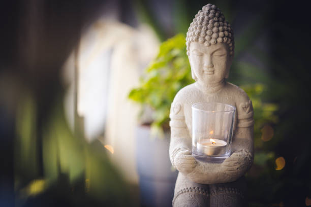 Zen spiritual ritual meditating white face of Buddha, brown candle on green floral background. Religion concept, esoterics. Still life style. Home decor. Place for text, copy space. Spiritual awakening