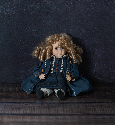 Amazing realistic vintage doll with blue eyes.The doll dressed in a blue dress and has a blond hair. Selective focus. Porcelain.