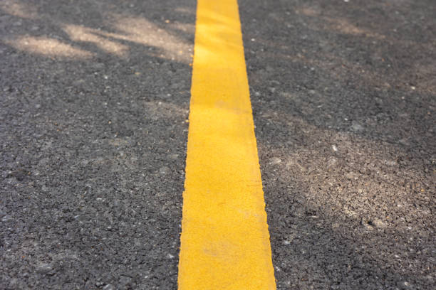 istock Close up yellow line on concrete road with rough surface under sunlight in the park shows concept of sign for driving lane, separating part and prohibition of transportation pathway. 1365138733
