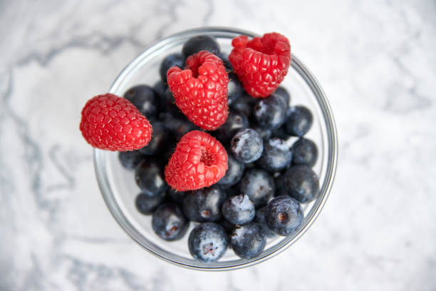Bowl with blueberries and fresh raspberries on a marble background. top view