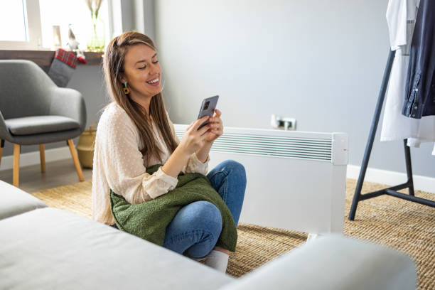 istock Woman and radiator using smartphone app for temperature control 1365146913