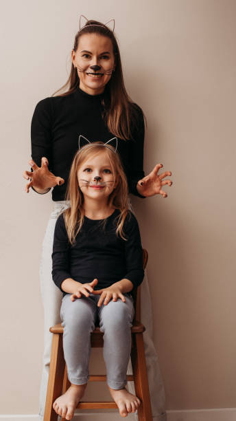 Family fun, face-painting cat mothers and daughter at wall Family fun, face-painting cat mothers and daughter at wall, funny and joy, home lifestyle, portrait, vertical cat face paint stock pictures, royalty-free photos & images