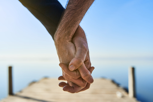 Valentine's day lgbt love concept. Gay gouple holding hands over wooden pier on blue sunny day