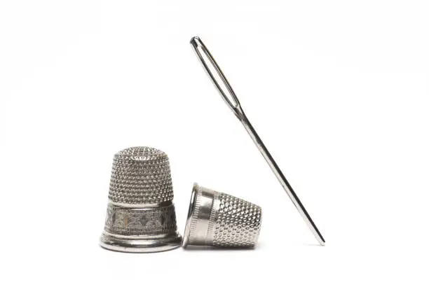 Close up sewing needle next to two different size thimbles on white background as concept for sewing tailoring and repairing clothes