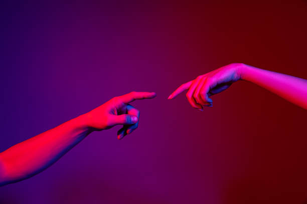 istock Two human hands trying to touch each other isolated on purple background in neon light. Concept of human relation, community, togetherness, symbolism, culture and history 1365149257