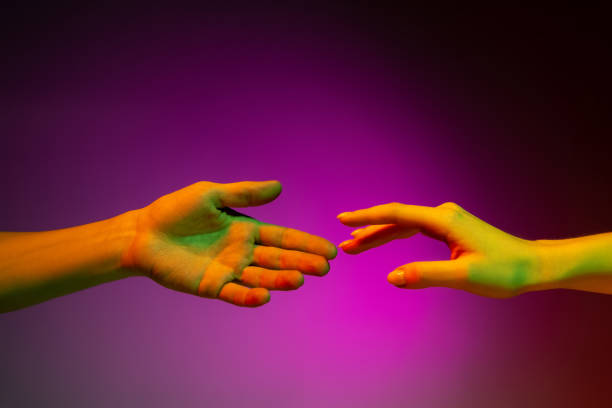istock Two human hands trying to touch each other isolated on purple studio background in neon light. Concept of human relation, community, togetherness 1365149260