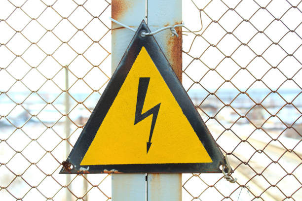 istock Sign - Caution electric voltage. Black lightning in the yellow triangle. Pedestrian bridge at the railway station. Close-up. 1365150776