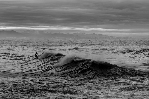 Black and white photo of a man on the waves of the sea in the city of Valencia. Spain.