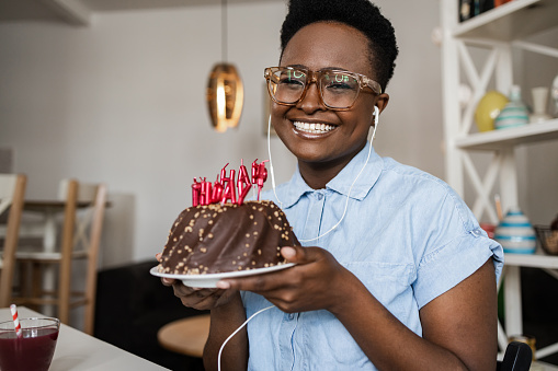 Young woman at home, holding a birthday cake and looking at camera