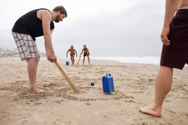 Two petanque sets in black cases with metallic boules and red target balls placed on red concrete edge near sand terrain, evoking relaxed outdoor sport in city environment