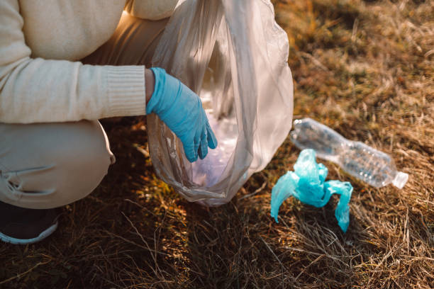 Earth day. Purity of nature. Female cleanup volunteer activist in rubber gloves hand puts a plastic bag trash in a garbage bag, collecting trash Earth day. Female activist hand puts a plastic trash in a garbage bag. Earth planet dirty and polluted. Environmental protection and waste reduction. earth day clean up stock pictures, royalty-free photos & images