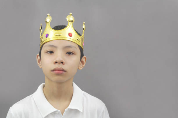 Positive Asian boy with gold king crown on head  smiling on gray background. Copy space for text.