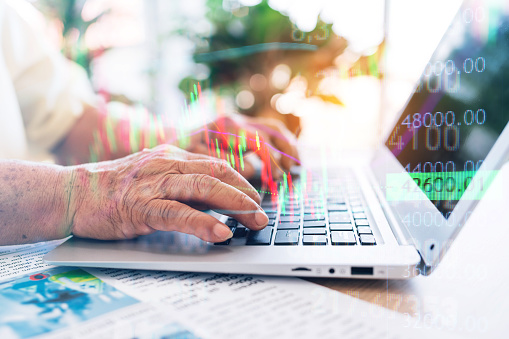 Close-up a senior retired old man using a laptop with hands pressing keyboard while sitting at home with market volatility chart. Trading stocks and crypto. Retirement investment concept.