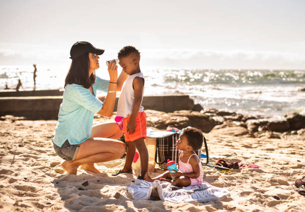 mama spendet ihren kleinen kindern am strand sonnencreme - african ethnicity brother ethnic little boys stock-fotos und bilder