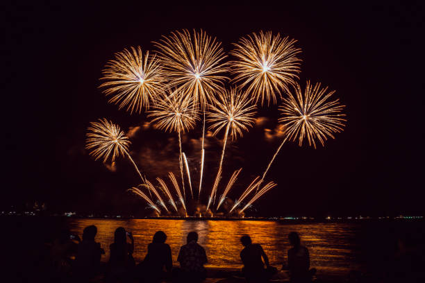 Festive beautiful colorful fireworks display on the sea beach, Amazing holiday fireworks party or any celebration event in the dark sky , Family sitting on the beach looking at fireworks stock photo