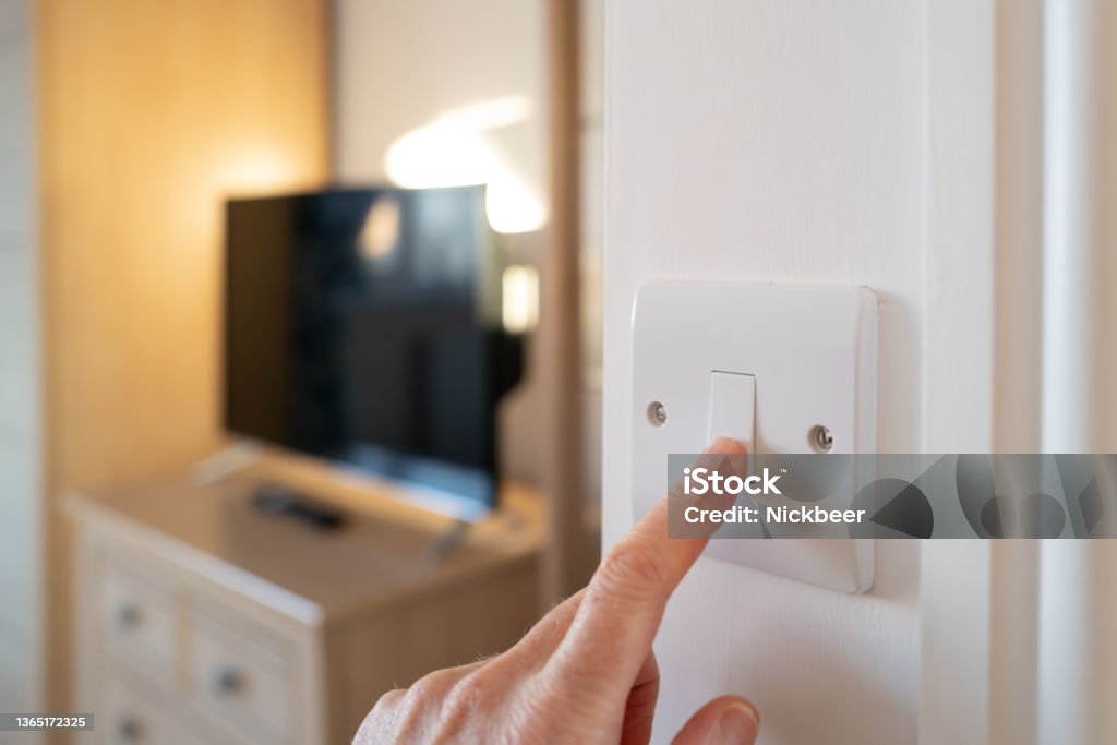 Shallow focus of a home owner switching off a bedroom light after waking up in late morning. Shallow focus of a home owner switching off a bedroom light after waking up in late morning. A smart TV can be seen in the room. Electricity Stock Photo