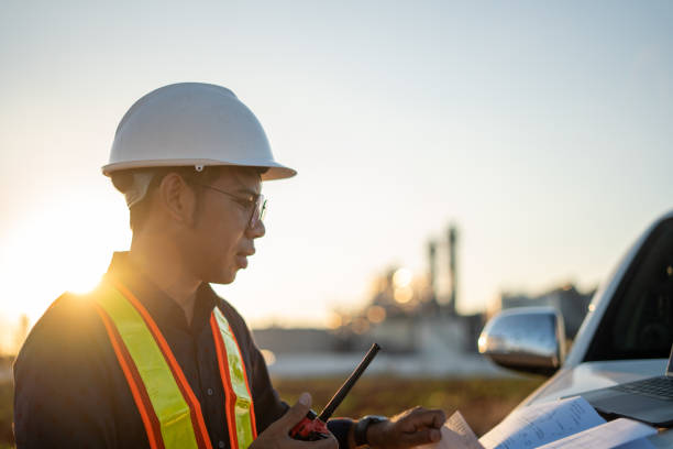 Engineer working with laptop and talking on walkie-talkie at construction site stock photo