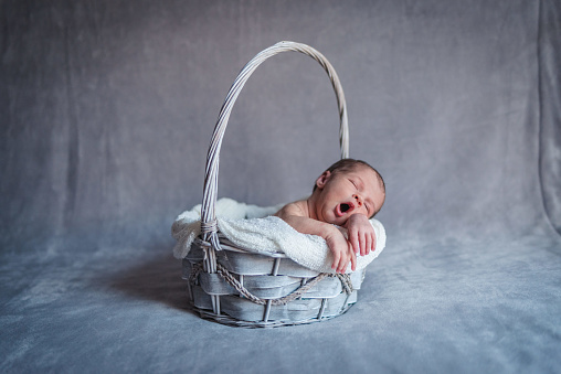 A newborn baby girl yawning while sleeping in a basket while sleeping. Newborn Session Concept