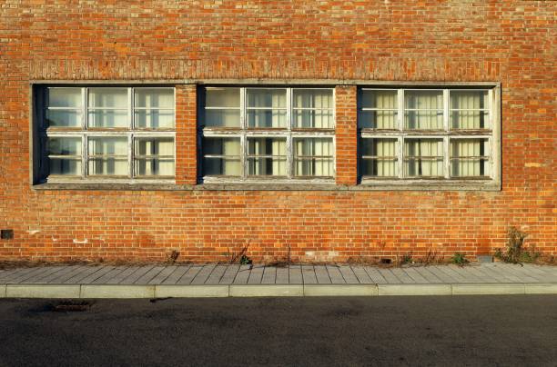 istock Brick wall with three large windows and curtains. Tiled concrete sidewalk and paved road in front. 1365176082