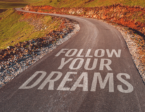 Follow your dreams motivational message on asphalt road through countryside landscape, selective focus